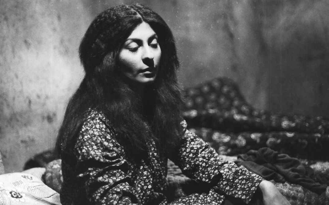 Film still from THE SEALED SOIL. A young woman with long hair sits in a room with half-closed eyes.