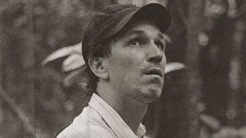 Portrait of Eduardo Williams with light shirt and cap looking up diagonally.