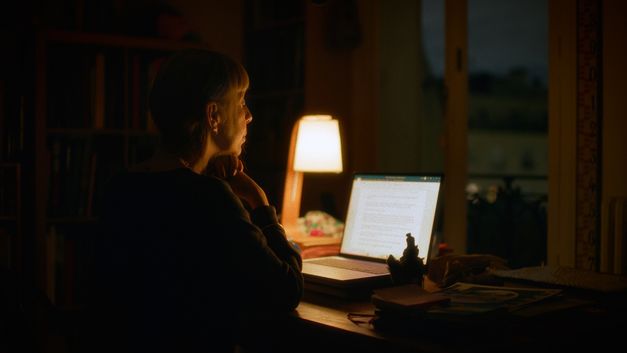 Frau sitzt nachts an einem Schreibtisch vor einem Laptop, nur von einer Tischlampe beleuchtet.