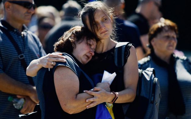 Film still from CHAS PIDLOTU (Time to the Target) by Vitaly Mansky. The image shows a close-up of two sad women hugging each other, surrounded by other people.