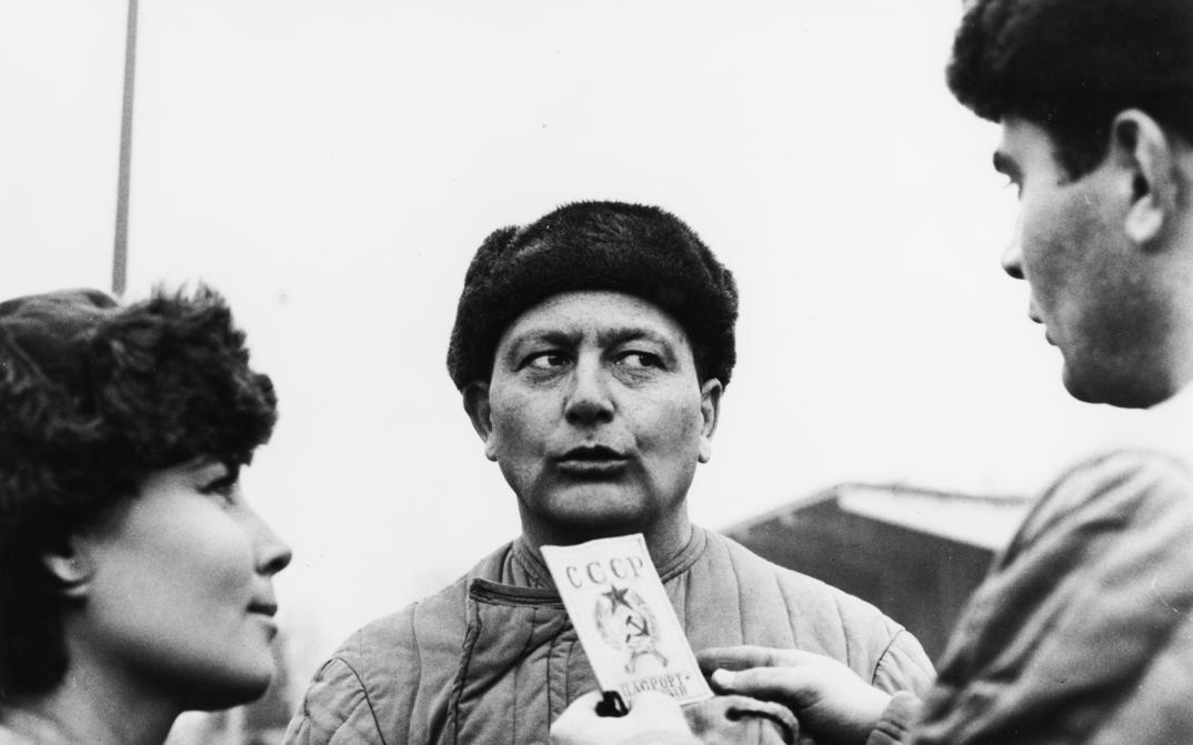 Film still from GENOSSE MÜNCHHAUSEN: Three people stand in the open, their faces turned towards each other.