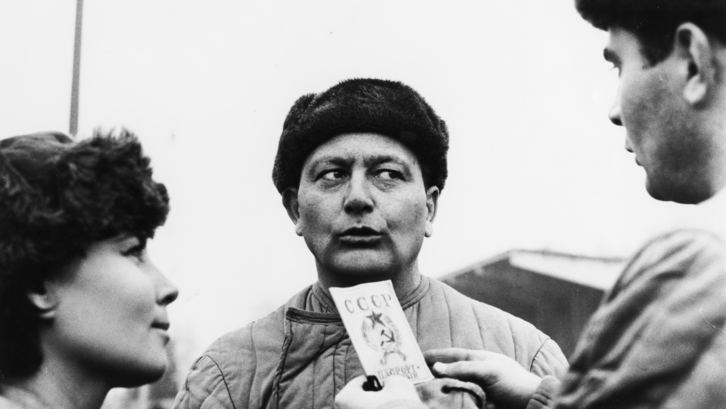 Film still from GENOSSE MÜNCHHAUSEN: Three people stand in the open, their faces turned towards each other.