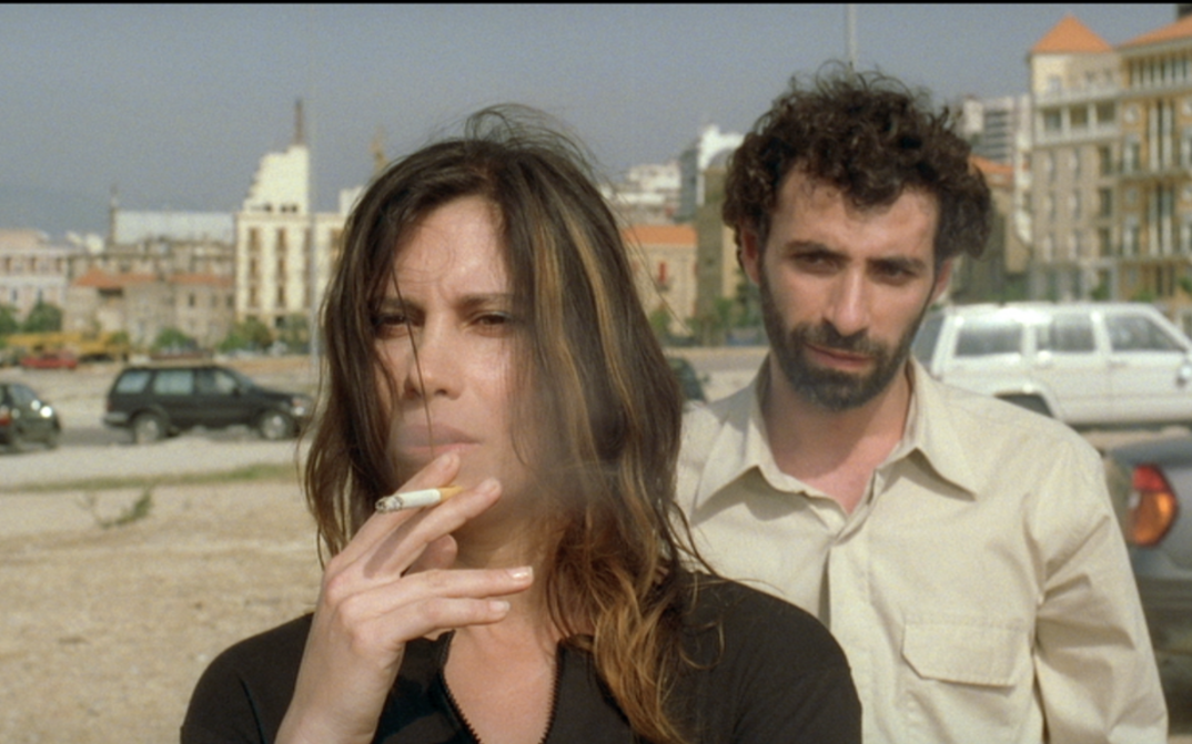 Filmstill aus TERRA INCOGNITA. Auf einer Straße steht rauchend eine Frau, hinter ihr steht ein Mann.
