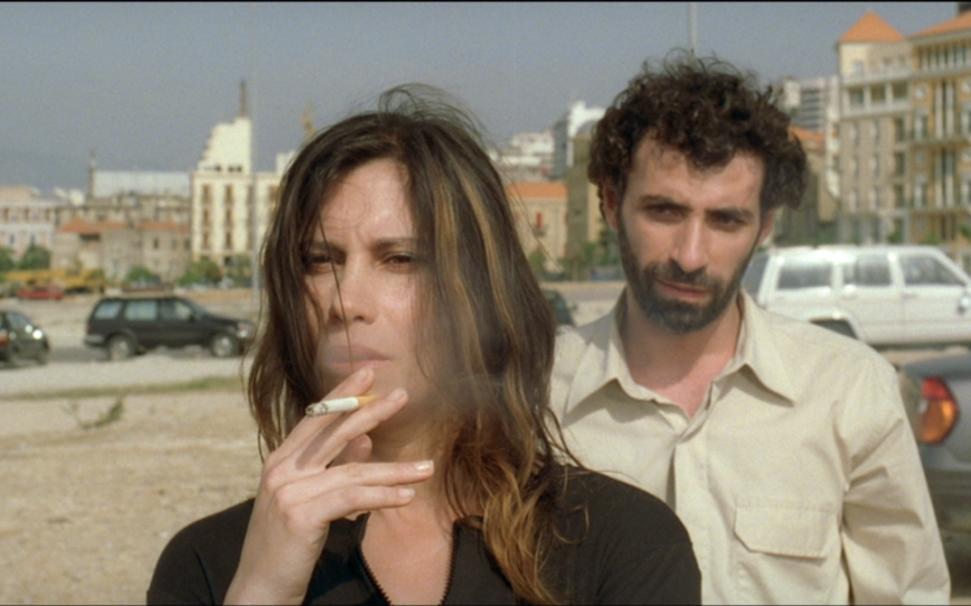 Filmstill aus TERRA INCOGNITA. Auf einer Straße steht rauchend eine Frau, hinter ihr steht ein Mann.