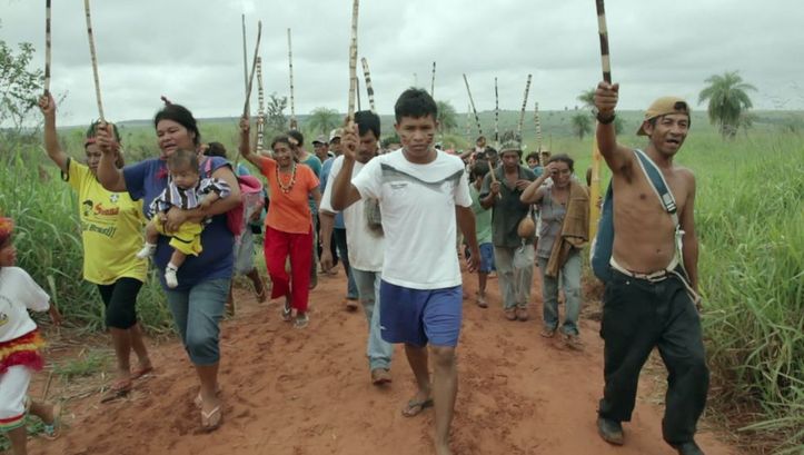 Filmstill aus MARTÍRIO: Eine Gruppe von Menschen geht mit erhobenen Stöcken einen Feldweg entlang.