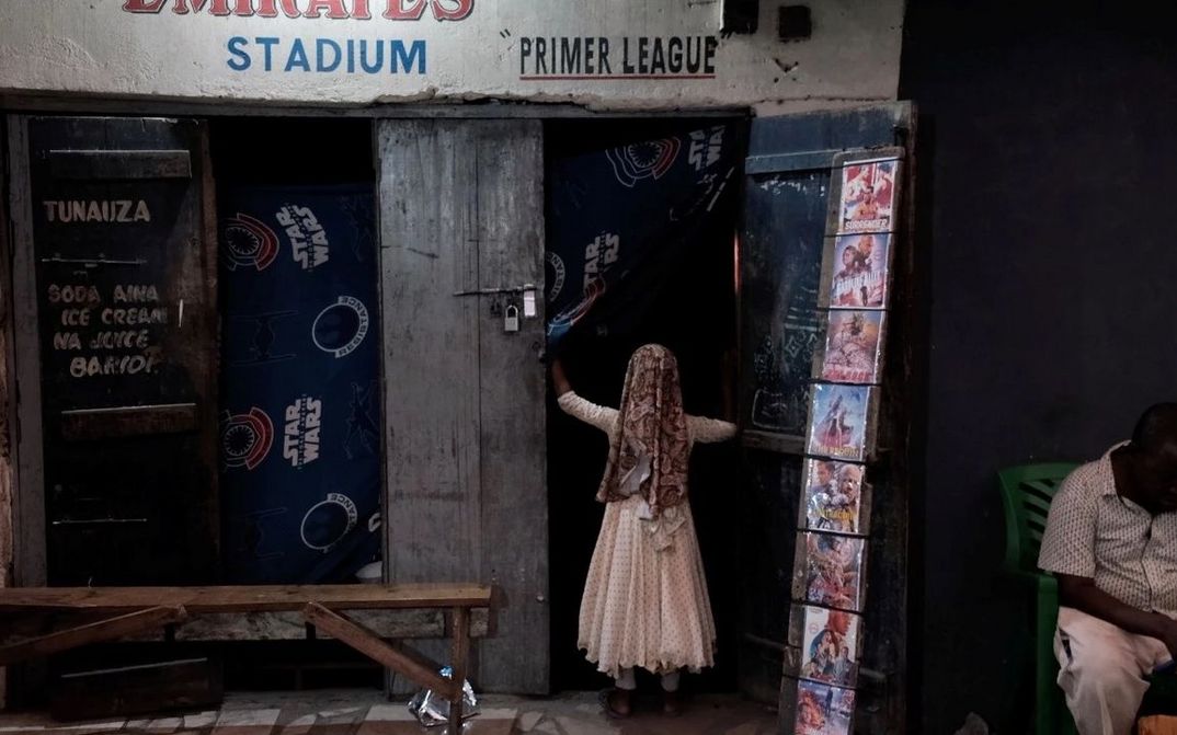 Film still from APOSTLES OF CINEMA: A child enters a simple store with movie posters hanging on the door.