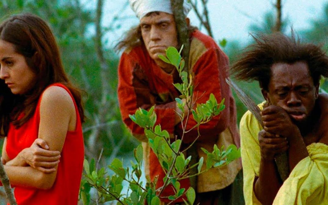Film still from MACUNAÍMA: Three people stand lost between trees and bushes.