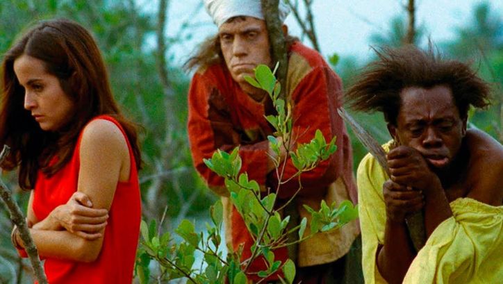 Film still from MACUNAÍMA: Three people stand lost between trees and bushes.
