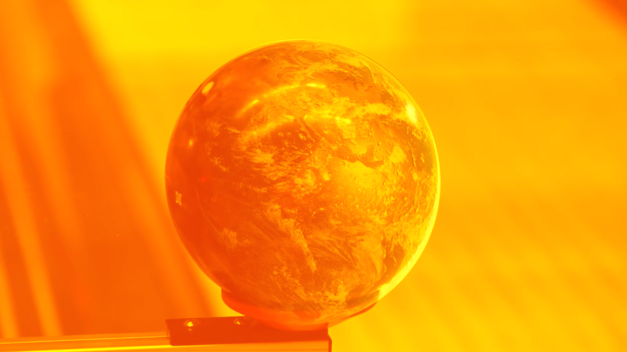 Filmstill aus STRANGE POWERS: Man sieht eine Weltkugel an einer Kante. Das gesamte Bild ist in leuchtend gelber und oranger Farbe. 