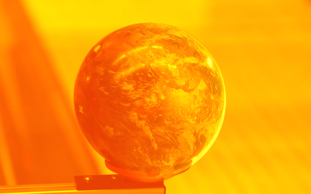 Film still from STRANGE POWERS: You can see a globe on a edge. The entire picture is a bright yellow and orange color. 