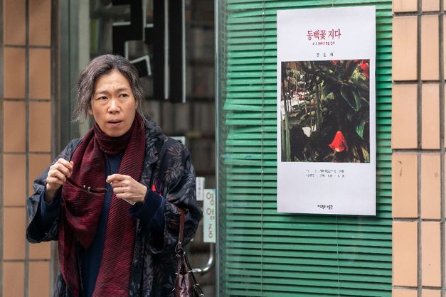 Eine Frau steht vor einem Schaufenster mit einem Plakat und einer grünen Jalousie und hält eine Brille in der Hand.