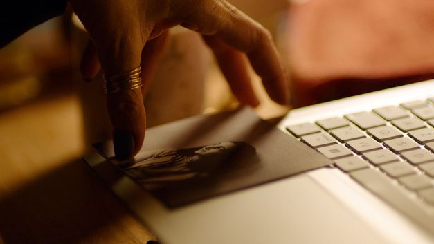 Nahaufnahme einer Hand mit Ring, die ein altes Foto auf dem Trackpad eines Laptops ablegt.
