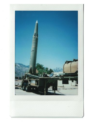 Polaroid of a vertical green missile in a display, with mountains in the background.