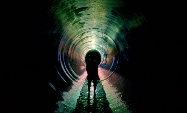 Film still from UNDERGROUND by Kaori Oda. The image shows the outline of a person in a long, dark tunnel. 