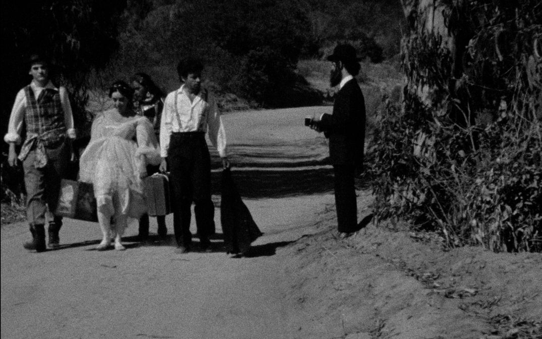 Filmstill aus THE MAN WITHOUT A WORLD: Ein paar Menschen gehen mit ihren Koffern eine Straße entlang.