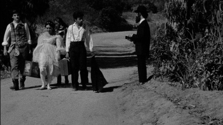 Film still from THE MAN WITHOUT A WORLD: A few people are walking down a street with their suitcases.