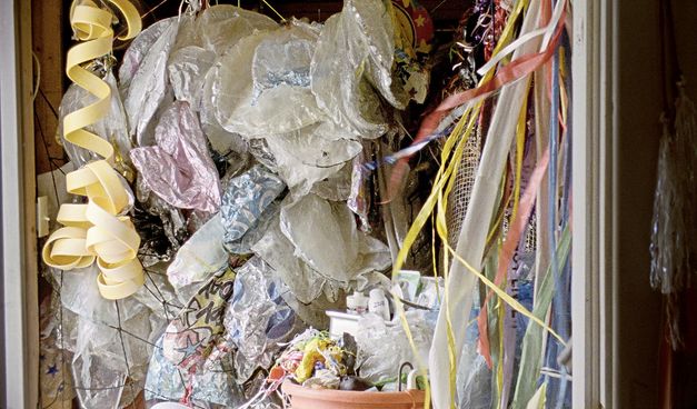 Filmstill aus „Geographies of Solitude“ von Jacquelyn Mills. Sicht in einen Schrank, in dem viele bunte Schnüre, Netze und alte Ballons, die ihre Luft verloren haben, hängen.