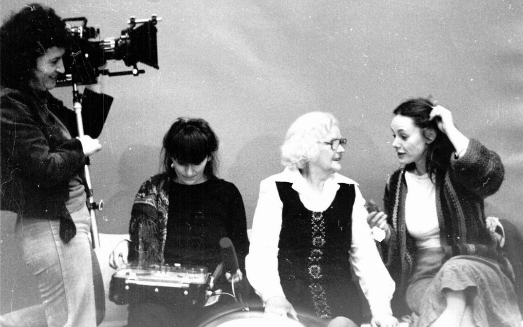 Set photo from the movie MULLE. Director Lilly Grote is standing on the left with a camera. Three women are sitting on a sofa and talking.
