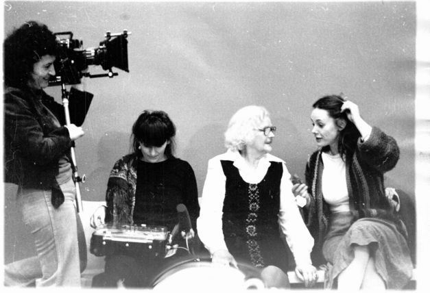 Set photo from the movie MULLE. Director Lilly Grote is standing on the left with a camera. Three women are sitting on a sofa and talking.