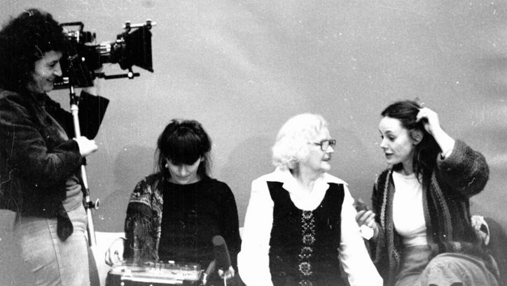 Set photo from the movie MULLE. Director Lilly Grote is standing on the left with a camera. Three women are sitting on a sofa and talking.