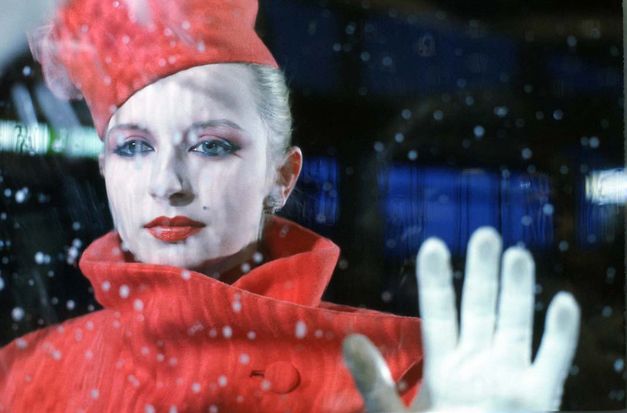 Film still from BILDNIS EINER TRINKERIN. An elegantly dressed woman looks through a pane of glass, you can see raindrops.