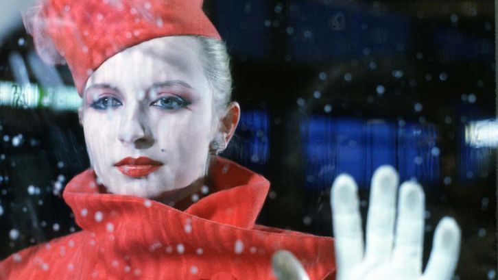 Film still from BILDNIS EINER TRINKERIN. An elegantly dressed woman looks through a pane of glass, you can see raindrops.