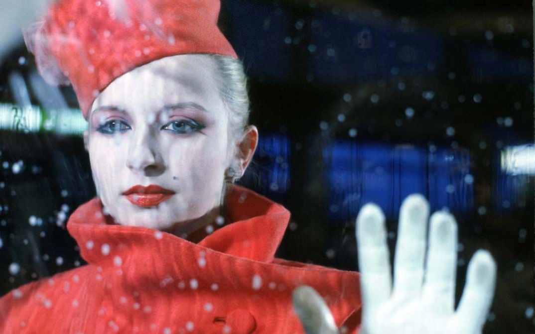 Filmstill aus BILDNIS EINER TRINKERIN. Eine elegant gekleidete Frau blickt durch eine Glasscheibe, man sieht Regentropfen.