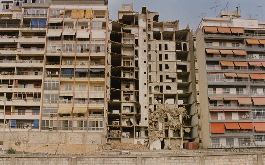 Film still from NOS GUERRES IMPRUDENTES. View of three apartment blocks, the middle one destroyed.
