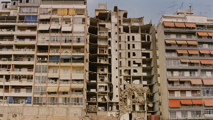 Film still from NOS GUERRES IMPRUDENTES. View of three apartment blocks, the middle one destroyed.