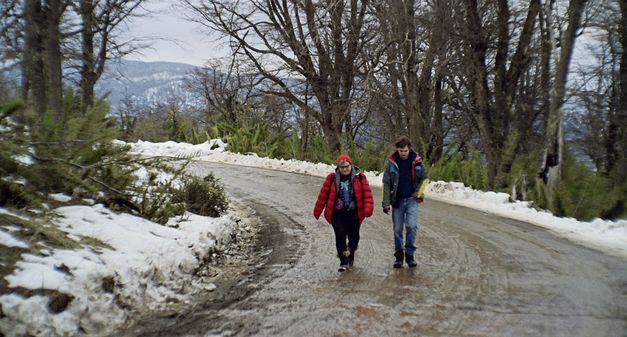 Filmstill from „Arturo a los 30" by Martín Shanly. Two people are walking down a snowy mountain road.