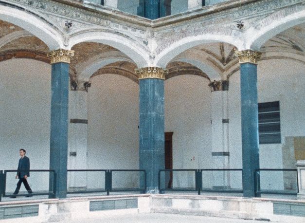 Filmstill aus BÖSE ZU SEIN IST AUCH EIN BEWEIS VON GEFÜHL: Auf einer Galerie im Gropius Bau geht ein Mann entlang.