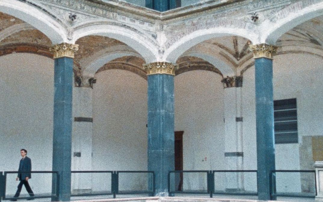 Filmstill aus BÖSE ZU SEIN IST AUCH EIN BEWEIS VON GEFÜHL: Auf einer Galerie im Gropius Bau geht ein Mann entlang.
