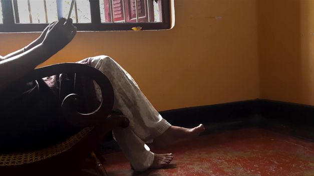 Still from the film "If from Every Tongue It Drips" by Sharlene Bamboat. A person sits in an armchair, their face cannot be seen.