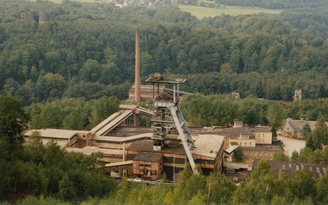 Film still from DIE WISMUT: The plant of a mining company surrounded by trees.