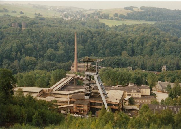 Filmstill aus DIE WISMUT: Die Anlage eines Bergbauunternehmens inmitten von Bäumen.