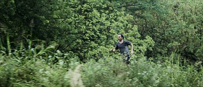 Still from the film "Camuflaje (Camouflage)" by Jonathan Perel. A man runs through an overgrown meadow, behind him the forrest. 