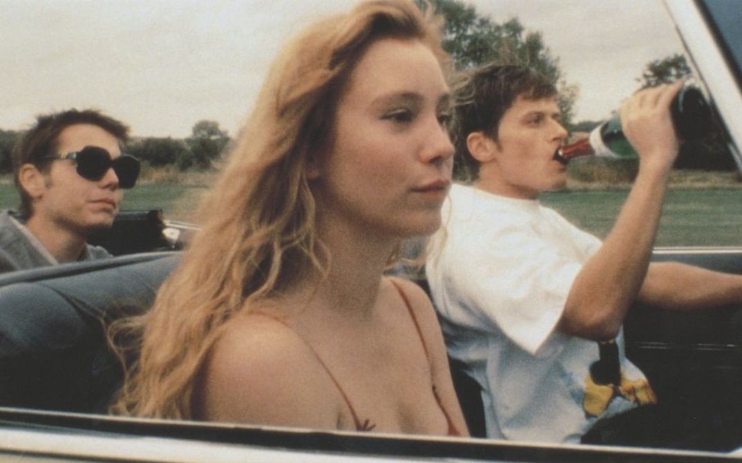 Filmstill aus VERGISS AMERIKA: Drei junge Menschen sitzen in einem Auto, der Fahrer trinkt Sekt aus der Flasche.