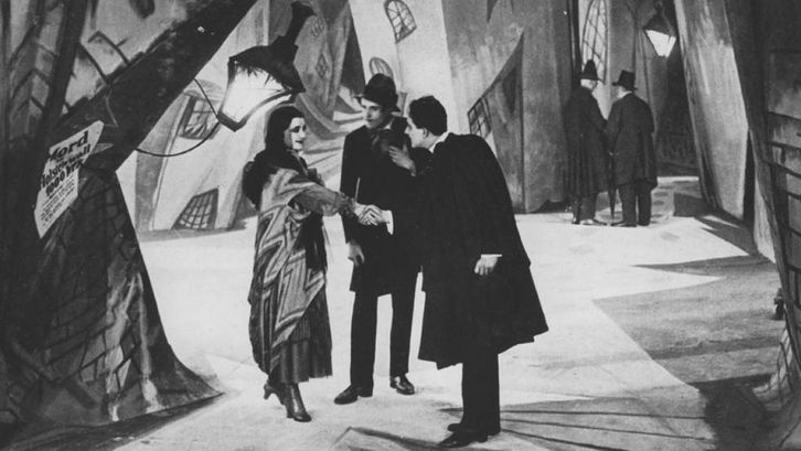 Film still from DAS CABINET DES DR. CALIGARI: A street scene with painted backdrops. A man and a woman shake hands. 