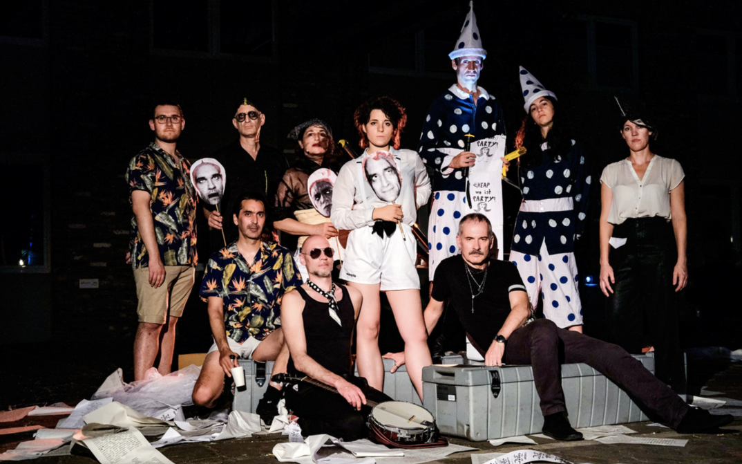 Filmstill aus CHEAP PEOPLE ARE OTHER PEOPLE: Eine Gruppe von Menschen, teilweise kostümiert, posiert auf einer Bühne.