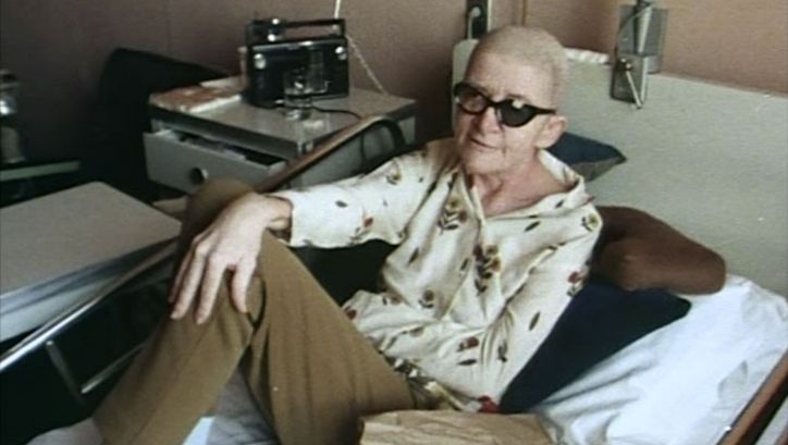 Film still from DYING: A person is sitting in a hospital bed.