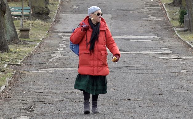 Film still from HELKE SANDER: AUFRÄUMEN: Helke Sander is walking down a street, wearing sunglasses, a cap and a red anorak.