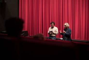 Eugene Green vor rotem Kinovorhang mit Mikrofon 