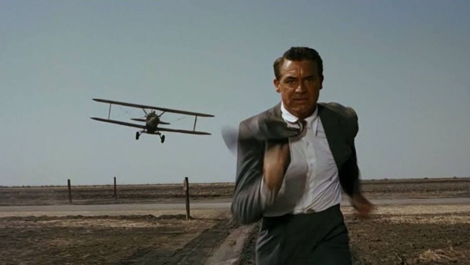 Film still from NORTH BY NORTHWEST:  man in a suit is running across a field; he is being chased by a small plane.