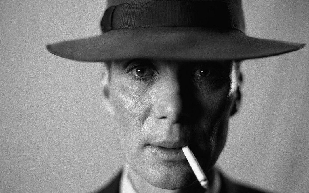 Filmstill aus OPPENHEIMER: Nahaufnahme des Schauspielers Cillian Murphy als Oppenheimer. Er trägt einen Hut, hat eine Zigarette im Mundwinkel und blickt frontal in die Kamera.