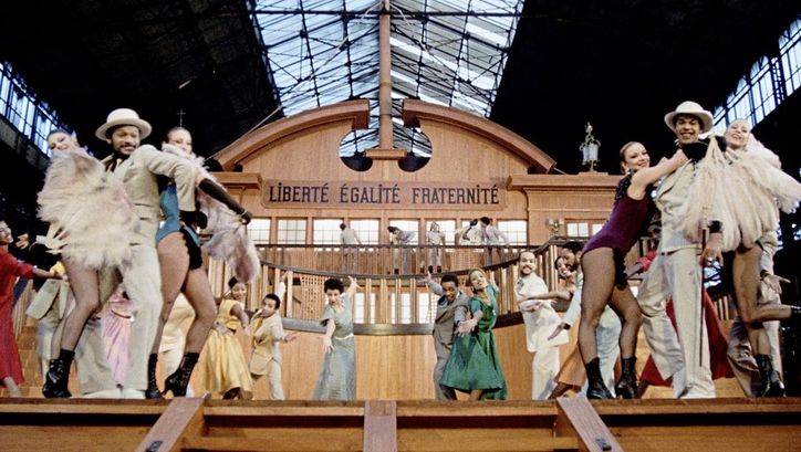 Still from the film "West Indies" by Med Hondo. We see a group of men and women dancers facing the camera while standing on a replica slave ship bearing the words "Liberté Égalité, Fraternité"