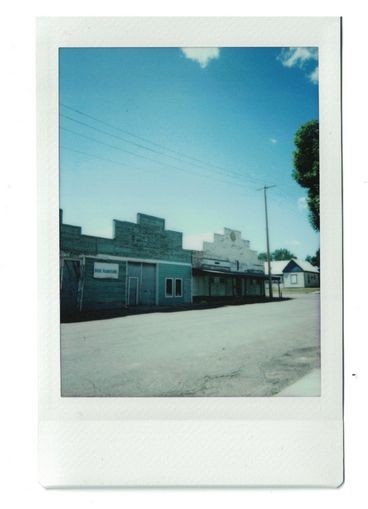 Polaroid of old storefronts on a rural street, against a blue sky.