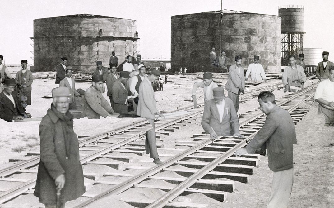 Film still from Sanaz Sohrabi’s "Sahnehaye Estekhraj". A collage with industrial buildings, railroad tracks and working men.