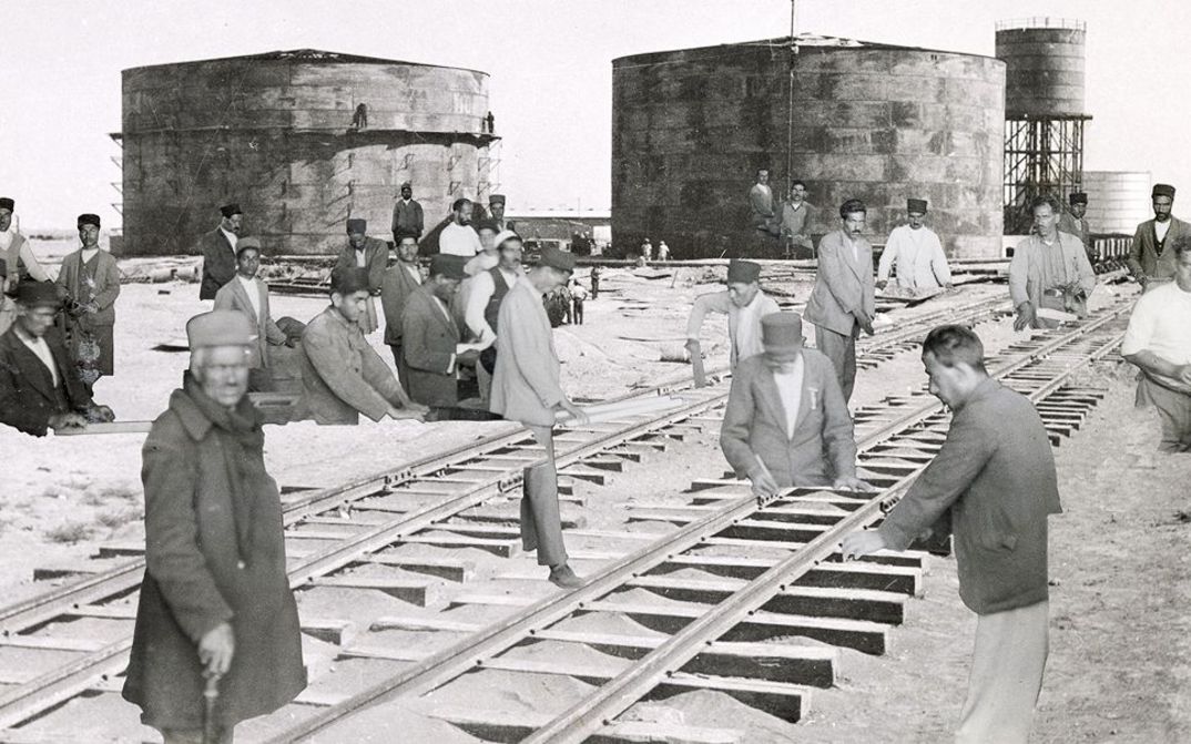 Film still from Sanaz Sohrabi’s "Sahnehaye Estekhraj". A collage with industrial buildings, railroad tracks and working men.