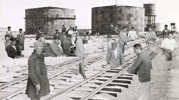 Film still from Sanaz Sohrabi’s "Sahnehaye Estekhraj". A collage with industrial buildings, railroad tracks and working men.