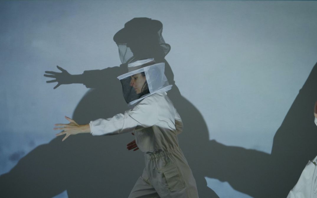 Film still from WHERE GRAVITY FADES: A person wearing a white beekeeper